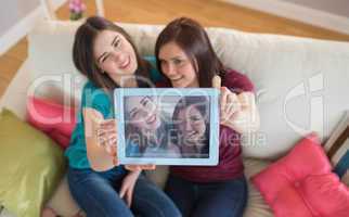 Two smiling friends on the couch taking a selfie with tablet pc