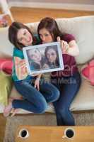 Two pretty friends on the couch taking a selfie with tablet pc