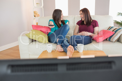 Two happy friends on the couch watching tv together