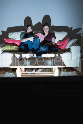 Two happy friends on the couch watching tv together in the dark