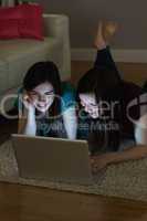 Two friends lying on floor using laptop together in the dark