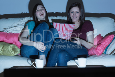 Two laughing friends on the couch watching tv together in the da