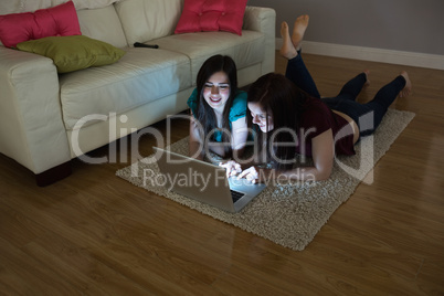 Two happy friends lying on floor using laptop together in the da