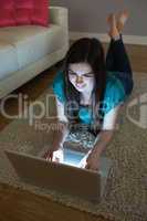 Happy brunette lying on floor using laptop in the dark