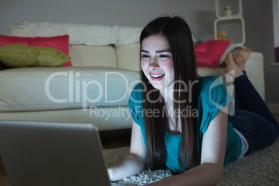 Smiling brunette lying on floor using laptop in the dark