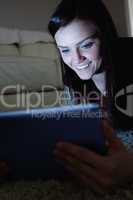 Smiling brunette lying on floor using tablet pc in the dark