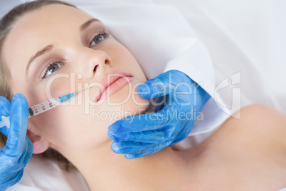 Surgeon making injection above lips on young woman lying
