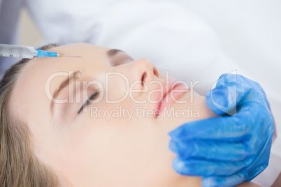 Surgeon making injection on forehead on content woman lying