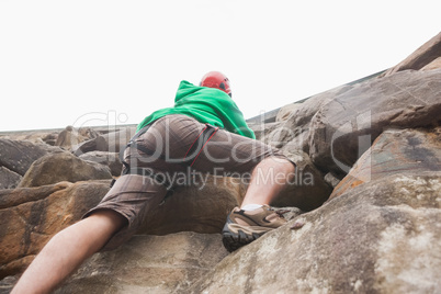 Determined man ascending a large rock face and seeing the top
