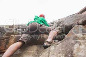 Determined man ascending a large rock face and seeing the top