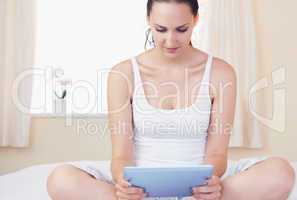 Content brunette sitting on bed using her tablet pc