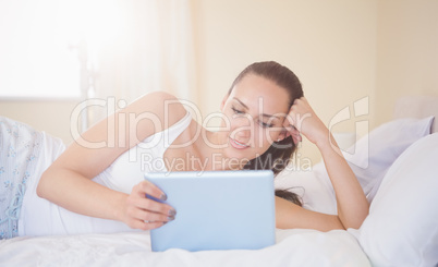 Content brunette lying on bed using her tablet pc