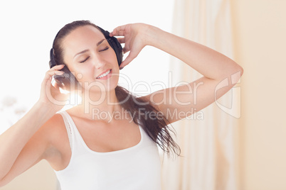 Happy brunette sitting on bed listening to music