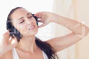 Relaxed brunette sitting on bed listening to music
