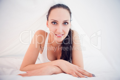Beautiful brunette lying under the sheets smiling at camera