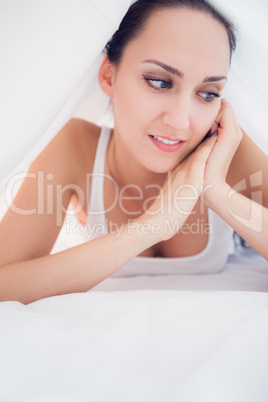 Happy brunette lying under the sheets looking away
