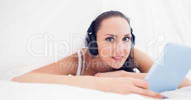 Happy brunette lying under the sheets listening to music using h