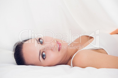 Happy brunette lying under the sheets looking at the camera
