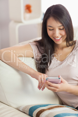 Happy asian girl using her smartphone on the couch