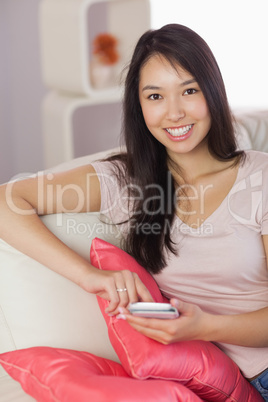 Happy asian girl using her smartphone on the couch looking at ca