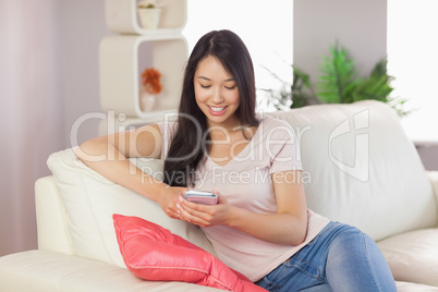 Pretty asian girl using her smartphone on the couch