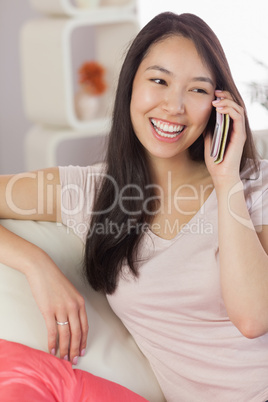 Pretty asian girl talking on her smartphone on the couch