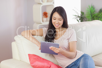 Happy asian girl using her tablet on the couch