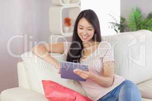 Happy asian girl using her tablet on the couch