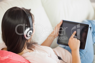 Girl using her tablet pc on the couch and listening to music