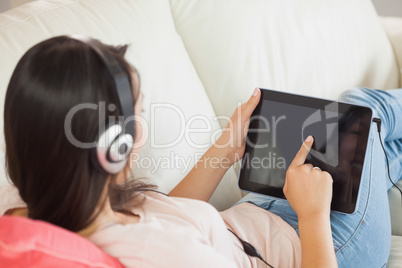 Girl using her tablet pc on the sofa and listening to music