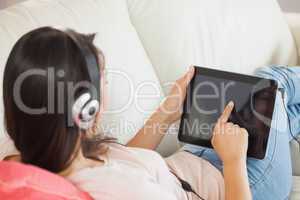 Girl using her tablet pc on the sofa and listening to music