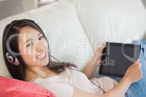 Girl using her tablet pc on the sofa and listening to music smil