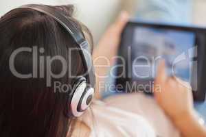 Girl using her tablet on the sofa and listening to music