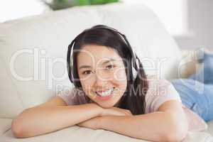 Smiling asian girl lying on the sofa and listening to music