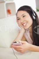 Happy asian girl lying on the sofa and listening to music with s