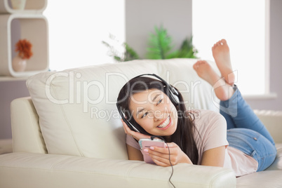 Smiling asian girl lying on the sofa and listening to music with