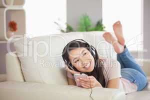 Smiling asian girl lying on the sofa and listening to music with