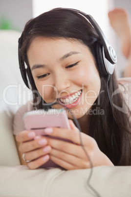 Cheerful asian girl lying on the sofa and listening to music wit