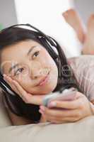 Cheerful asian girl lying on the sofa and listening to music wit