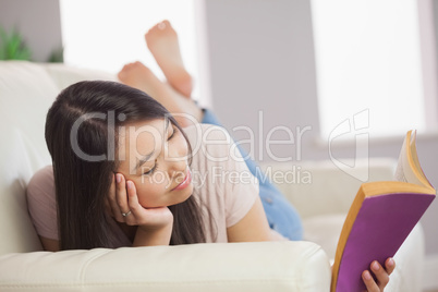 Peaceful asian girl lying on the sofa reading book