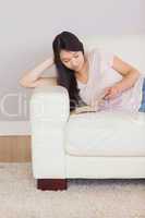 Content asian girl lying on the sofa reading book