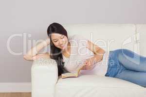 Pretty asian girl lying on the sofa reading book