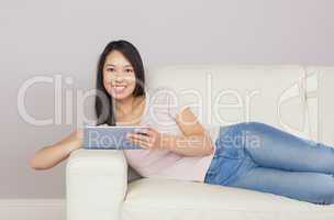 Pretty asian girl lying on the sofa using digital tablet smiling