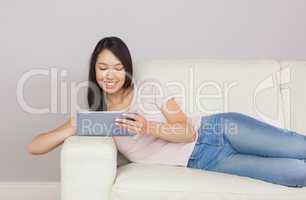 Pretty asian girl lying on the sofa using digital tablet