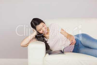 Pretty asian girl lying on the sofa reading a magazine