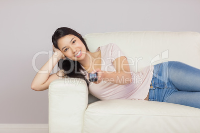 Cheerful asian girl lying on the couch watching tv