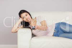 Cheerful asian girl lying on the couch watching tv