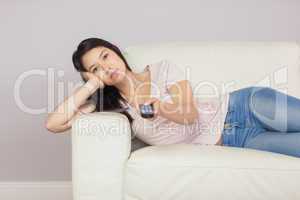Bored asian girl lying on the couch watching tv