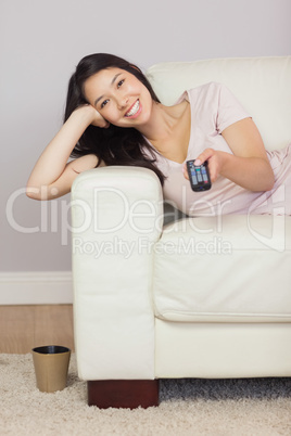 Happy asian girl lying on the sofa watching tv