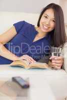 Pretty asian girl lying on the sofa reading a novel and drinking